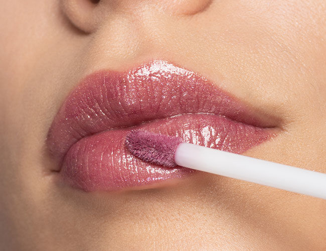 Ein rose-farbiger Lip Gloss wird auf die Lippen aufgetragen
