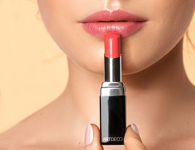 Ein orangefarbiger Lippenstift von Artdeco wird von einem Model vor ihren Lippen gehalten