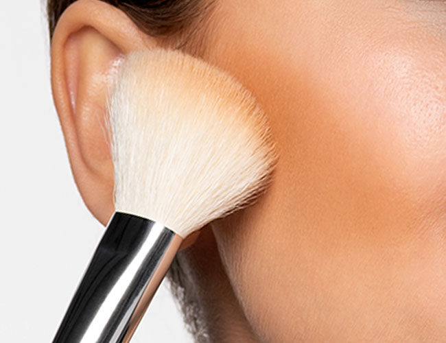 Bronzer is applied to a cheekbone with a brush